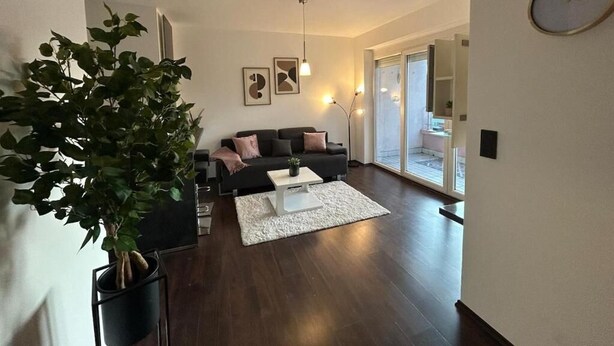 A modern living room with a dark wood floor, a white coffee table, a black sofa with pink cushions, and a large plant. - FarawayHomes Studio Bruck 17 (Bruck an der Mur)