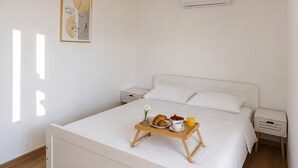 Un lit bien fait, avec un plateau contenant des articles pour le petit-déjeuner, du linge de lit blanc et une simple table de chevet.