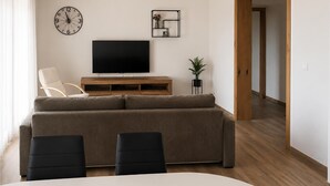 Un salon avec un canapé, des fauteuils, un téléviseur, une horloge et une plante.