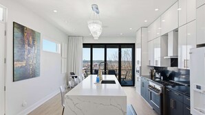 A modern kitchen with a marble island, stainless steel appliances, and a large window offering a city view. - Luxury Mt. Adams Retreat (Cincinnati)