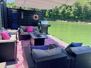 Un espace extérieur aménagé avec des meubles en osier, un barbecue et une vue sur un plan d’eau.