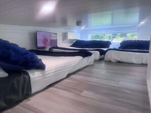 Habitación con tres camas alineadas, un televisor de pantalla plana en la pared y una ventana que deja entrar luz natural.