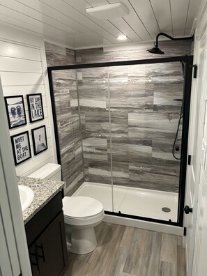 Un baño moderno con cabina de ducha, inodoro, lavabo de encimera de granito y fotografías enmarcadas en la pared.