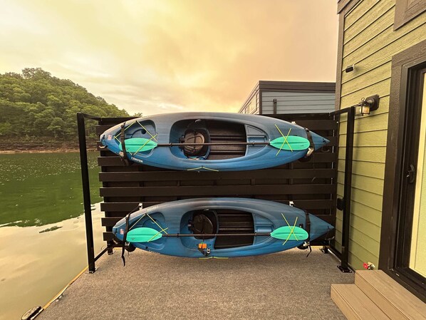 Dos kayaks sujetos a un soporte en la parte exterior de un edificio, con vistas a un lago y colinas.