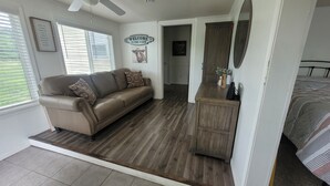 A room with a brown leather sofa, a wooden cabinet, a ceiling fan, and a bed with patterned bedding. - Kansas City 3-bedroom farmhouse on peaceful acreage near Legends entertainment! (Kansas City)