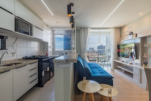 Eine moderne Küche mit integriertem Mikrowellenherd, einem Essbereich mit blauem Sofa und einem an der Wand befestigten Fernseher.