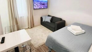 Una camera d'albergo con un letto, una poltrona, una televisione, una scrivania e una finestra con tende.