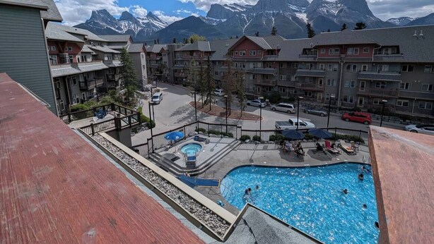 A residential area with a swimming pool, surrounded by apartment buildings, and a mountain range in the background. - Three Peaks Penthouse [3 Hot Tubs & Pool] (Canmore)
