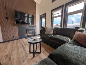 Ein modernes Wohnzimmer mit Kamin, einer Couch, einem kleinen runden Tisch und einem an der Wand befestigten Fernseher.