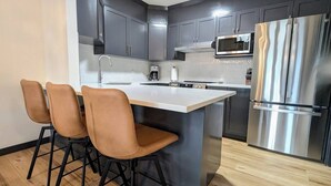 A modern kitchen with dark cabinets, a stainless steel refrigerator, and a central island with bar stools. - Three Peaks Penthouse [3 Hot Tubs & Pool] (Canmore)