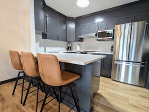 Eine moderne Küche mit dunklen Schränken, einem Edelstahl-Kühlschrank und einer zentralen Kochinsel mit Barhocker.