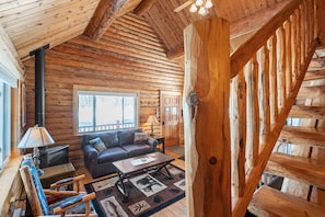 Ein Blockhaus-Interieur mit Kamin, Sofa, Couchtisch und Blick ins Freie.