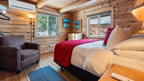 Camera da letto in una baita di legno, con un letto, una sedia, un comodino e una lampada.