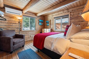 Ein Schlafzimmer einer Holzhütte mit einem Bett, einem Sessel, einem Nachttisch und einer Lampe.