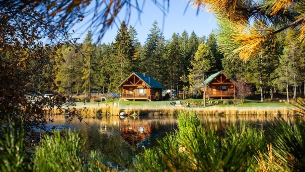 Una baita con veranda, uno stagno e una foresta circostante.