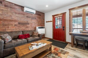 Ein Wohnzimmer mit einer Holzwand, einer rotem Tür, einem Sofa, einem Couchtisch und einem Fenster.