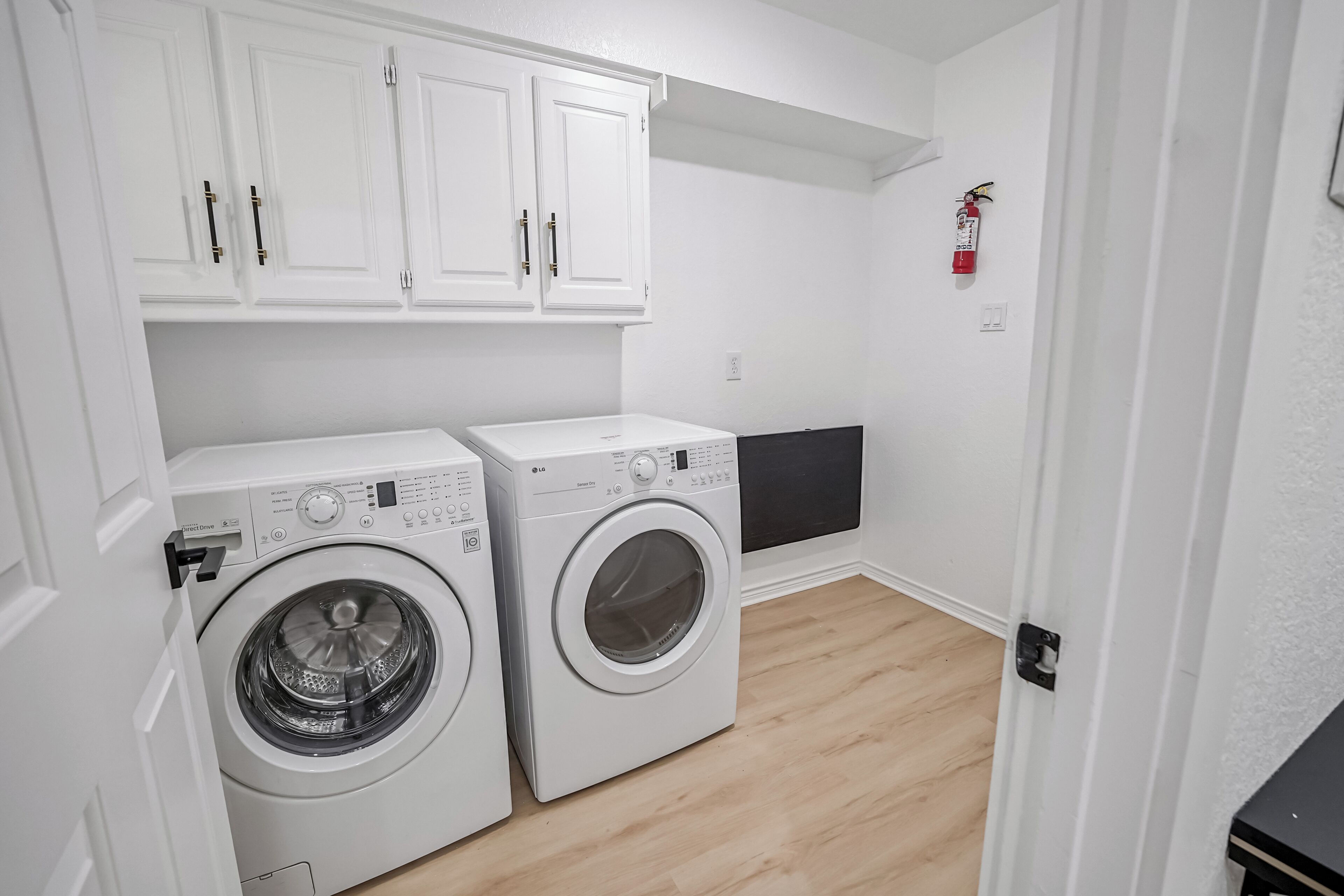 Een wasserette met twee witte wasmachines, witte kastjes en een brandblusser aan de muur.