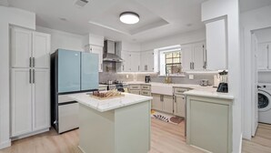 A modern kitchen with white cabinetry, a central island, a built-in oven, and a window providing natural light. - Paradiso in Frisco, A perfect home away from home in North, Dallas! (Frisco)