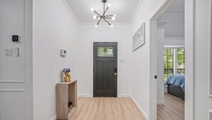 A hallway with a wooden floor, a dark door with a window, a light fixture, and a bed in the adjacent room. - Paradiso in Frisco, A perfect home away from home in North, Dallas! (Frisco)