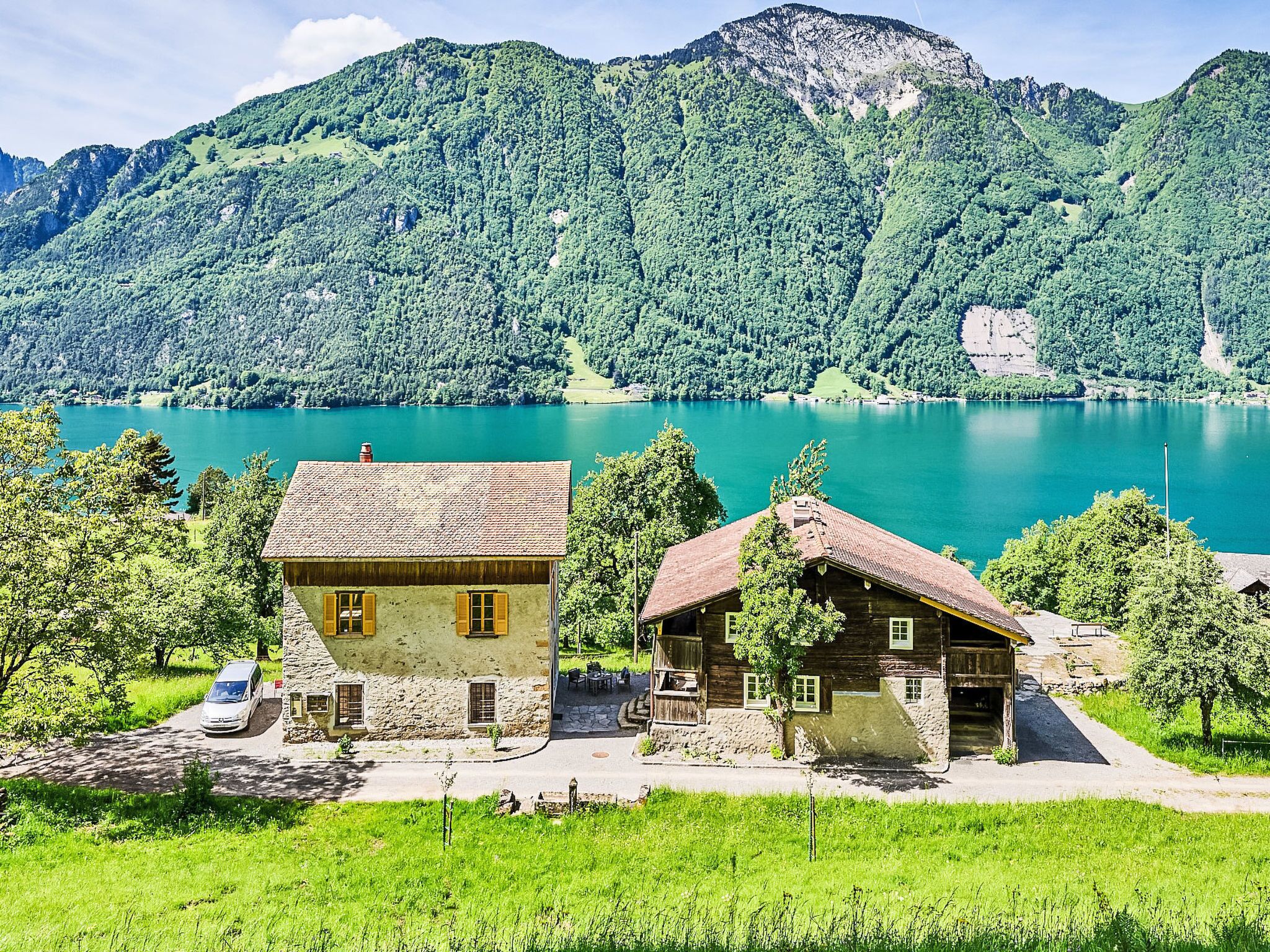 Eine Berglandschaft mit einem See und zwei rustikalen Gebäuden mit Steinmauern und Holzdächern.