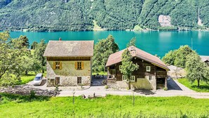 Eine Berglandschaft mit einem See und zwei rustikalen Gebäuden mit Steinmauern und Holzdächern.
