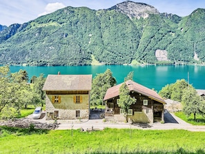 Eine Berglandschaft mit einem See und zwei rustikalen Gebäuden mit Steinmauern und Holzdächern.