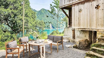Une terrasse en bois avec une table et des chaises, offrant une vue sur un lac et des montagnes boisées.