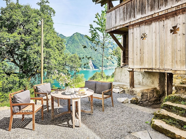 Eine Holzterrasse mit Tisch und Stühlen mit Blick auf einen See und bewaldete Berge.