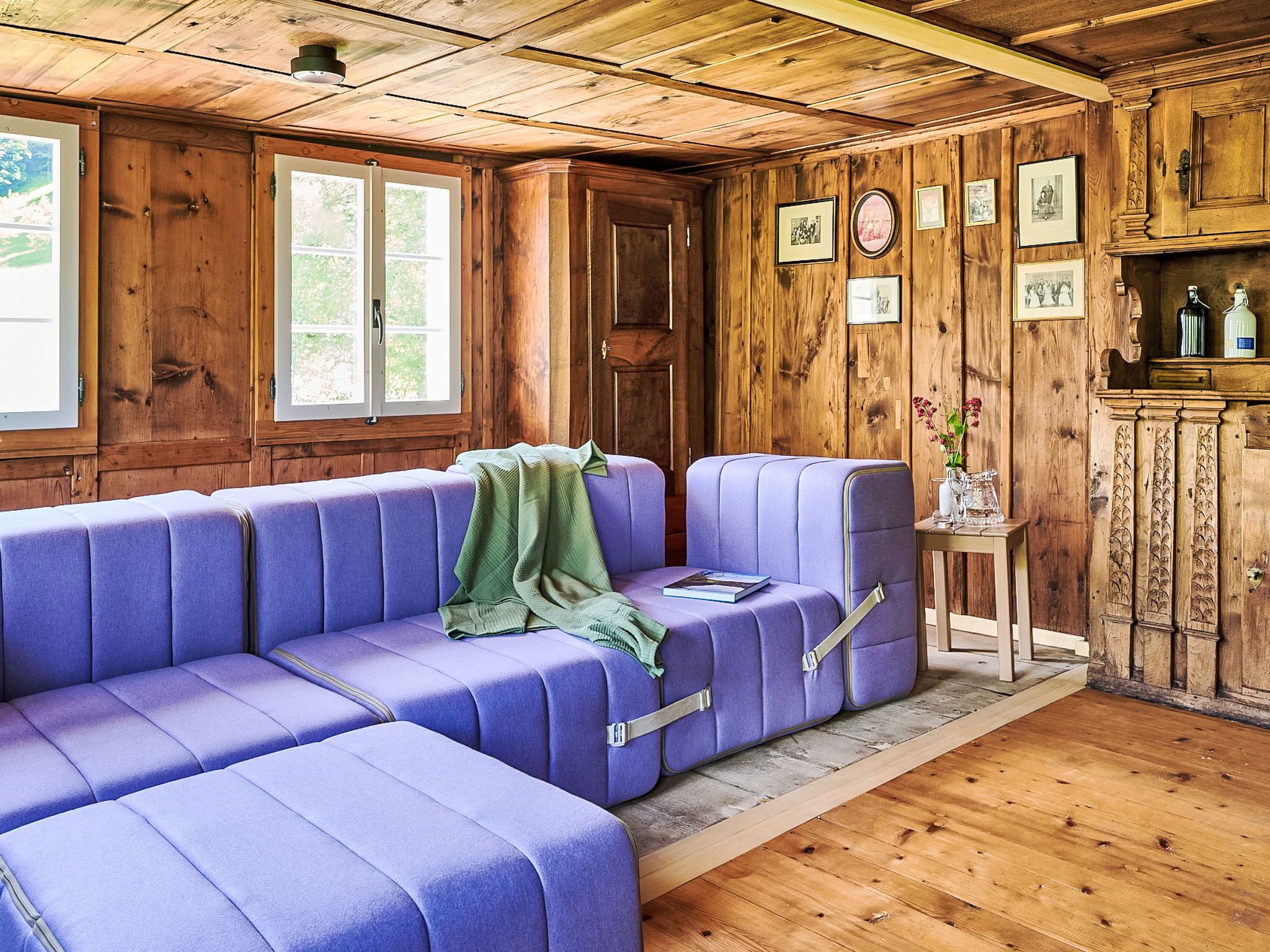 Une pièce avec un plafond en bois, un canapé violet, une porte et des tableaux encadrés accrochés au mur.