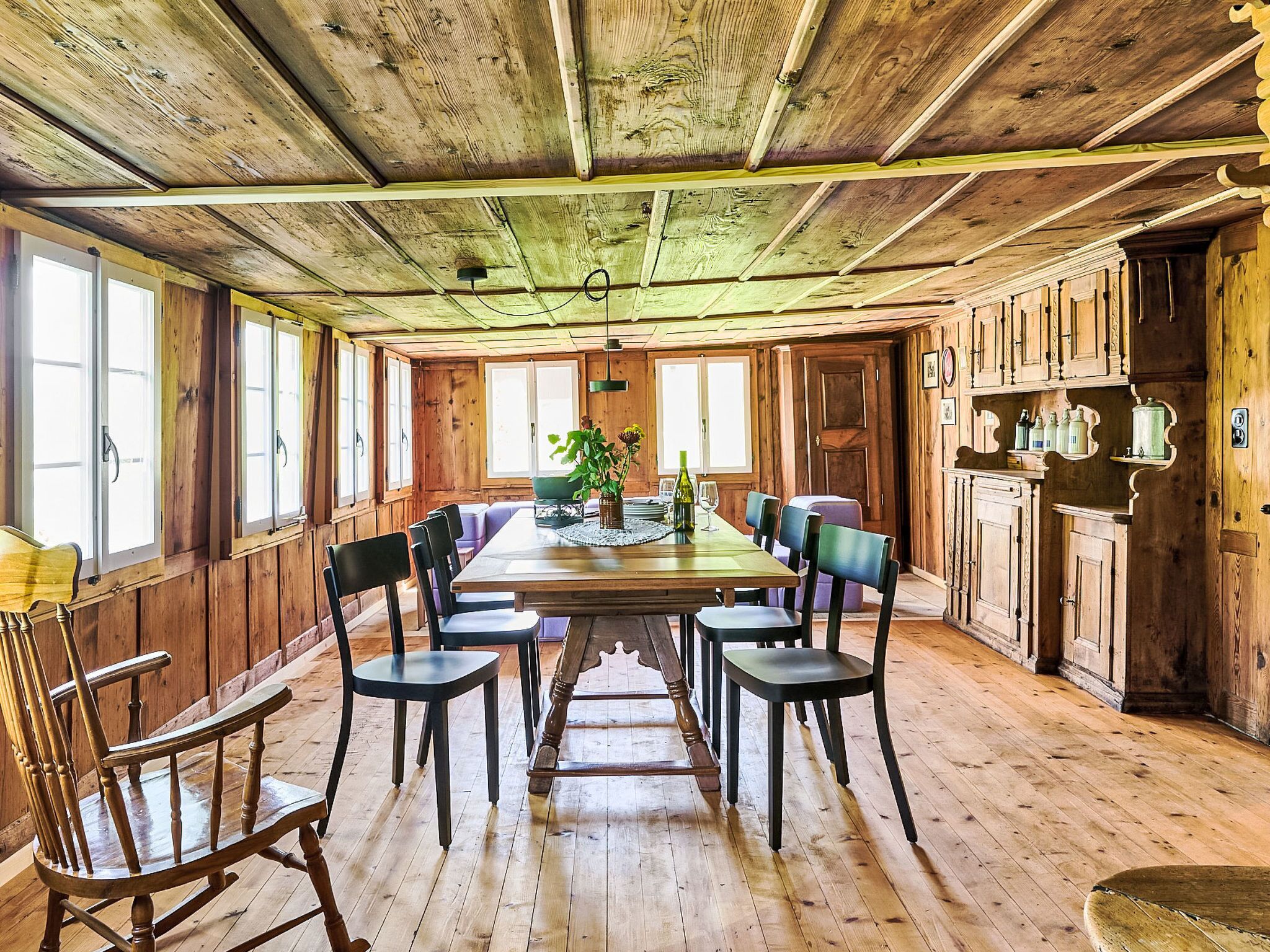 Une salle à manger en bois avec une longue table, des chaises et une plante en pot.