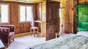Ein Zimmer in einer Holzhütte mit einem Bett, einem Sessel, einem Schreibtisch und einem grünen Schrank.