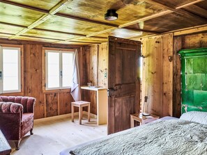 Ein Zimmer in einer Holzhütte mit einem Bett, einem Sessel, einem Schreibtisch und einem grünen Schrank.