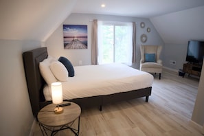 Un dormitorio con una cama, una silla, un televisor, una lámpara y un cuadro en la pared.