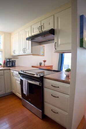 Una cocina con armarios blancos, horno de acero inoxidable, cafetera y ventana con vistas.