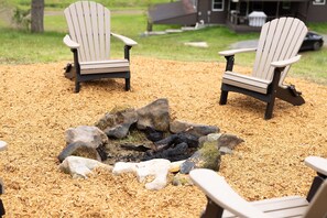 Dos sillas Adirondack alrededor de un brasero con piedras y virutas de madera en el suelo.