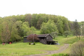 A rural house with a porch, a staircase, and a dirt path leading to it.