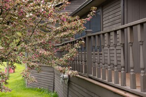 Une maison avec une clôture en bois, un arbre aux fleurs roses et une fenêtre avec un rideau.