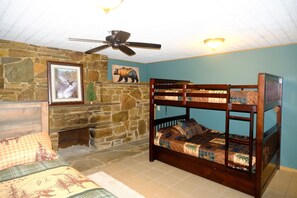 A room with a bunk bed, stone wall, fireplace, ceiling fan, and a framed picture.