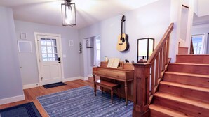 A room with a wooden staircase, a piano, a guitar, and a blue patterned rug. - The Homestead at Anderson Ridge |Pool & Trails (Schellsburg)