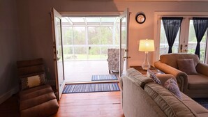 An open door leading to a balcony, a sofa, a chair, a lamp, and a clock on the wall. - The Homestead at Anderson Ridge |Pool & Trails (Schellsburg)