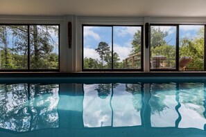 An indoor swimming pool with clear views of trees and a building outside through large windows. - La bergerie - ESCALANS (ESCALANS)