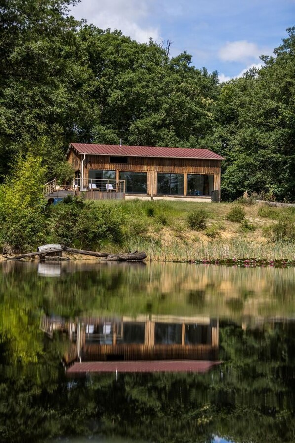 A wooden cabin with a red roof, situated by a lake with dense forest in the background. - La bergerie - ESCALANS (ESCALANS)
