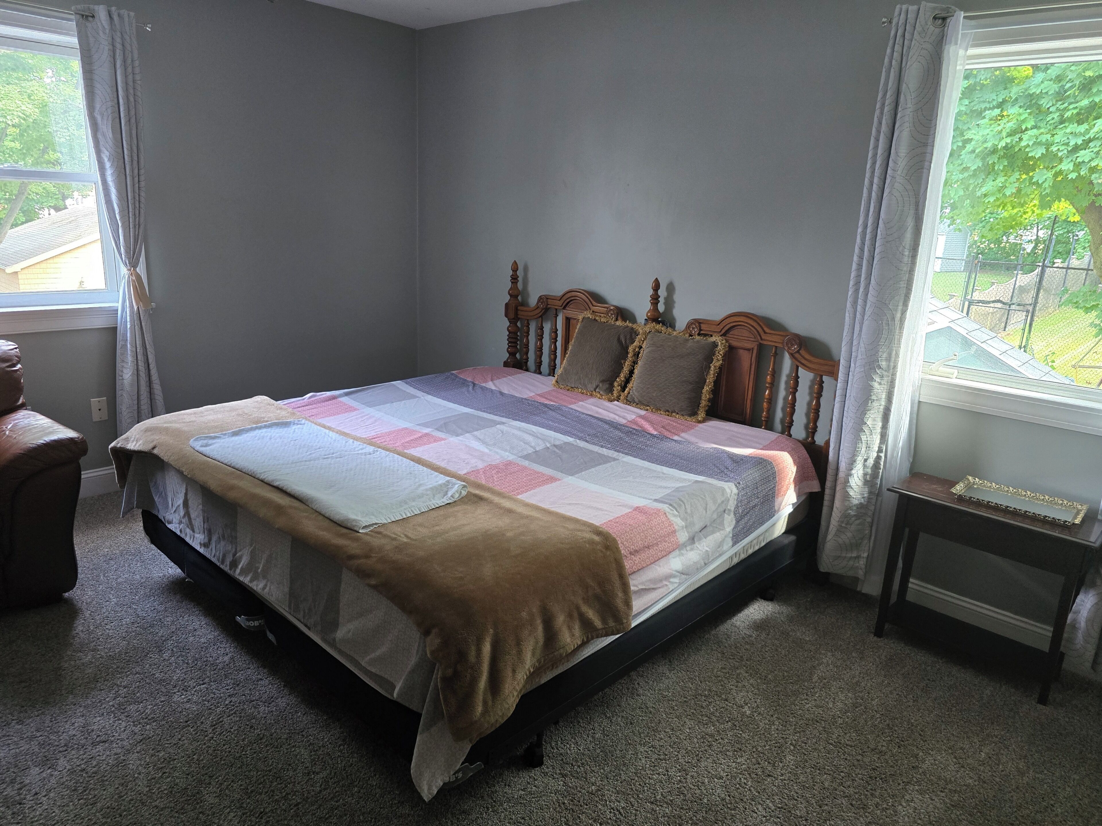 Un dormitorio con cama, ventana con cortinas, una mesita y una silla.