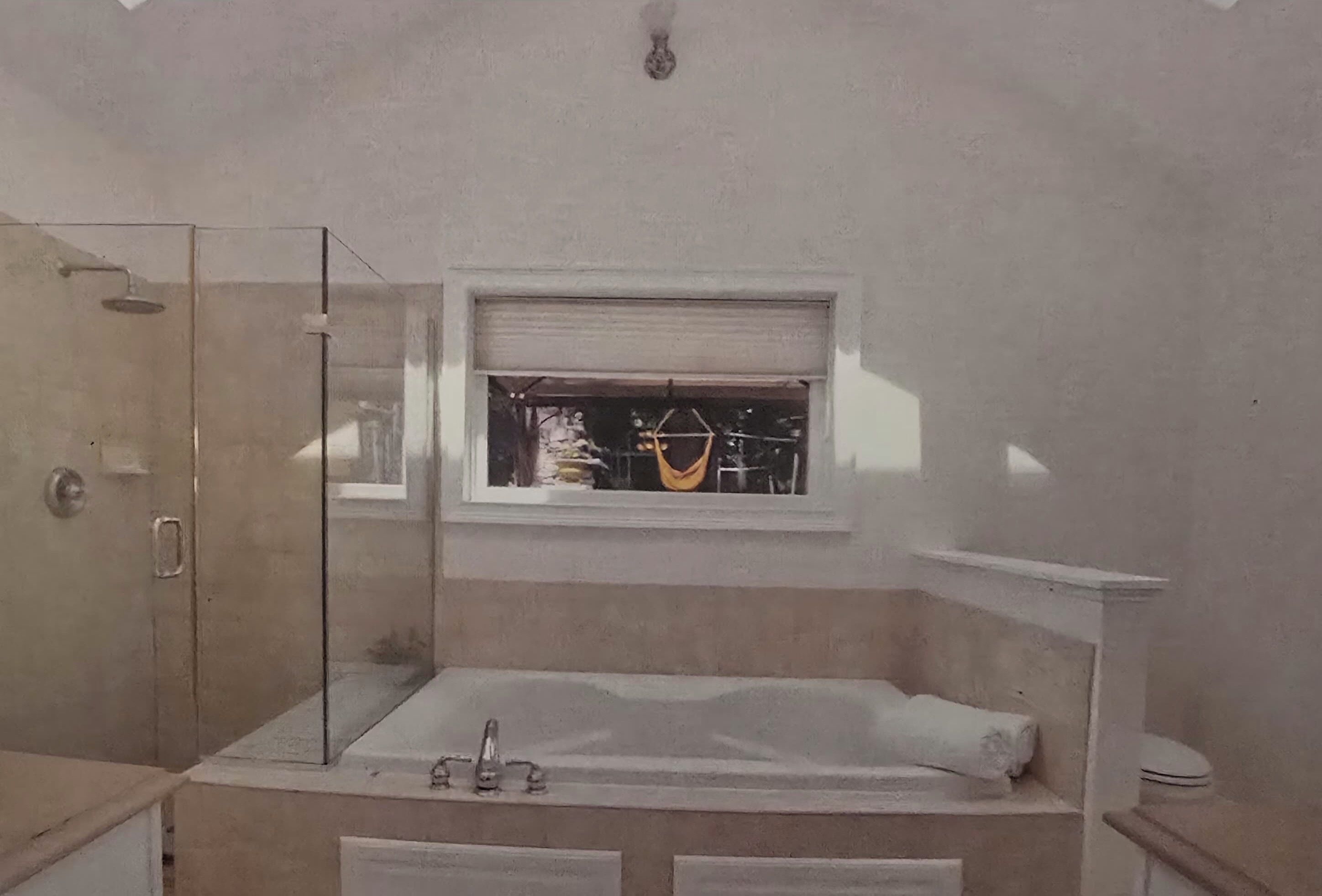 A bathroom with a glass shower enclosure, a bathtub, a window with blinds, and a toilet.