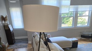 En stue med sofa, gulvlampe, sofabord med plante og udsigt til det fri gennem store vinduer.