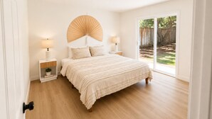 Ein Schlafzimmer mit einem Bett, Nachttischlampen, einem Wandventilator und einer Glastür zu einem Garten.