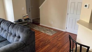 Ein Wohnzimmer mit grauem Sofa, Holzboden, Treppe und Tür.