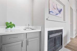 A modern kitchen with a white countertop, grey cabinets, a sink, and a fireplace.