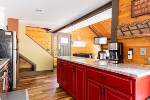 A kitchen with a wooden ceiling, a red cabinet, a coffee maker, and a television.