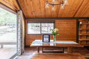 Un intérieur en bois avec une table, un panneau d’accueil encadré, un vase rempli de fleurs et une fenêtre donnant sur des arbres.